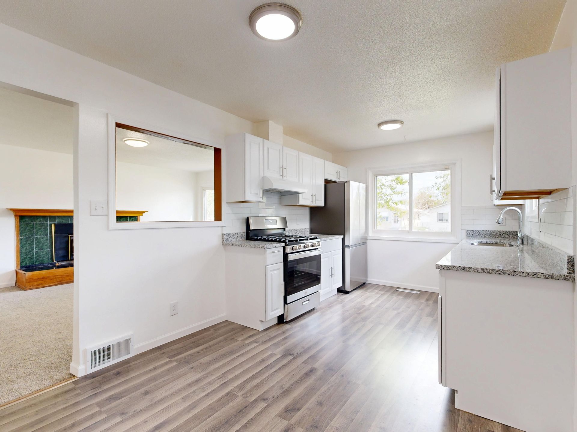 Bright, newly renovated kitchen featuring white cabinets, hardwood floors, and stainless steel appliances.